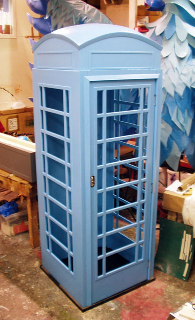 An old-style telephone box with glass doors. Painted in a primer coat of pale blue-grey