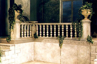 view of stage set - a stone courtyard with a stone balustrade and a large door with an arched fanlight above it. Ivy grows on the walls.